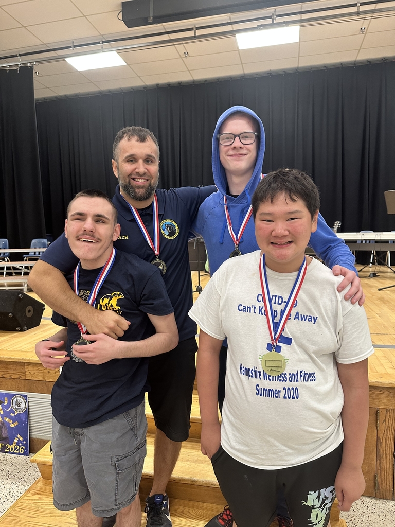 Mr. Smith poses with three male students with who are wearing medals of achievement around their neck.