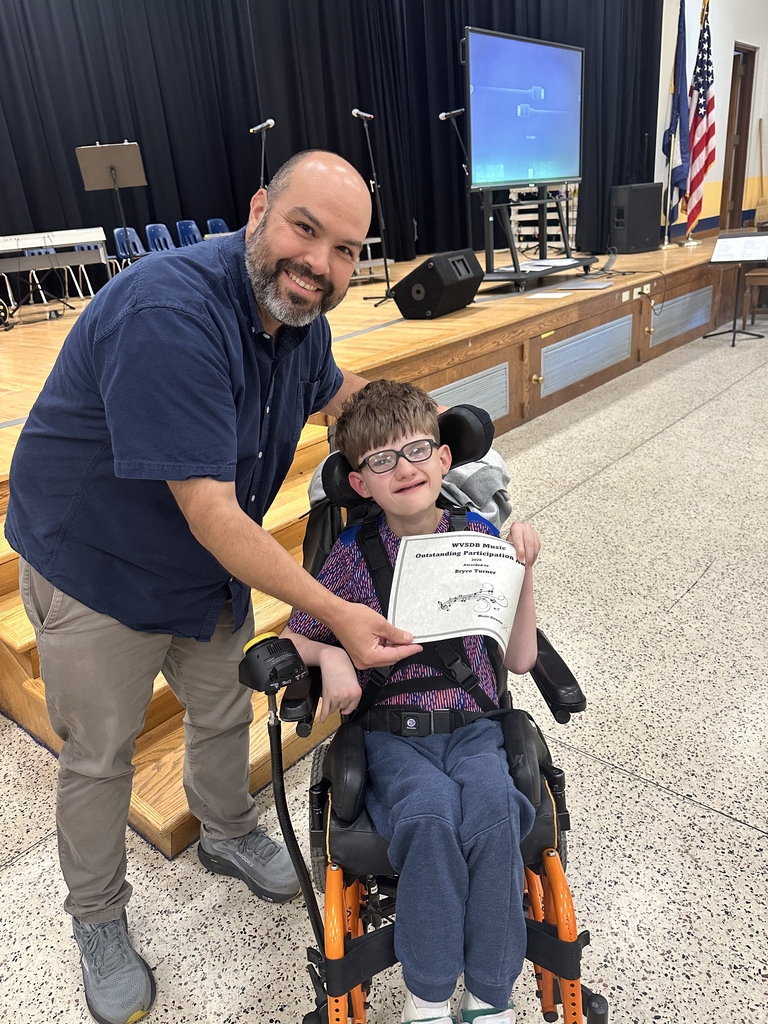 Mr. Haza, WVSDB Music Instructor, smiles and poses with a male student, Bryce, as Bryce holds up a certificate of achievement.