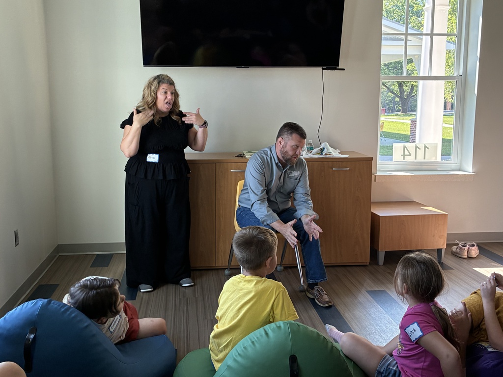 Superintendent Burch is seated with a female interpreter to his left. Attendees are seated on bean bag chairs during story hour.