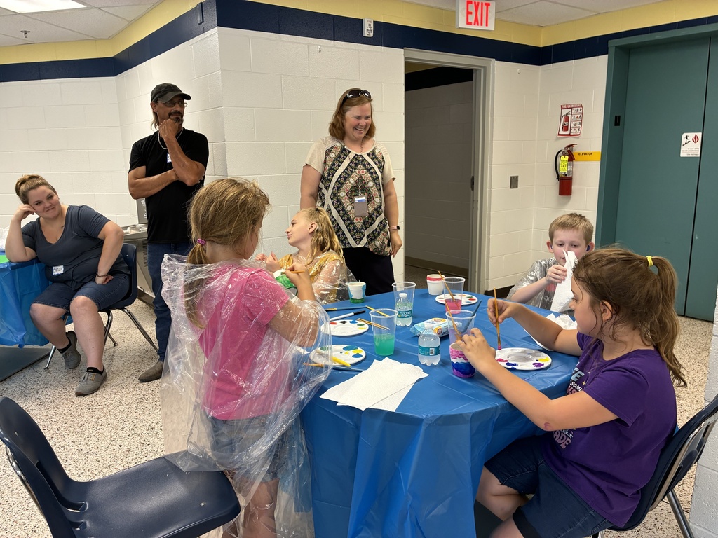 Dean Hesse laughs as she watches attendees craft while they are seated at a circular table with a blue tablecloth on top.