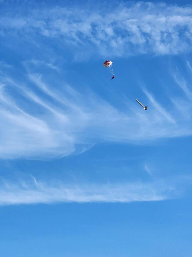 A rocket with a parachute attached to it glides down to the ground after its launch.