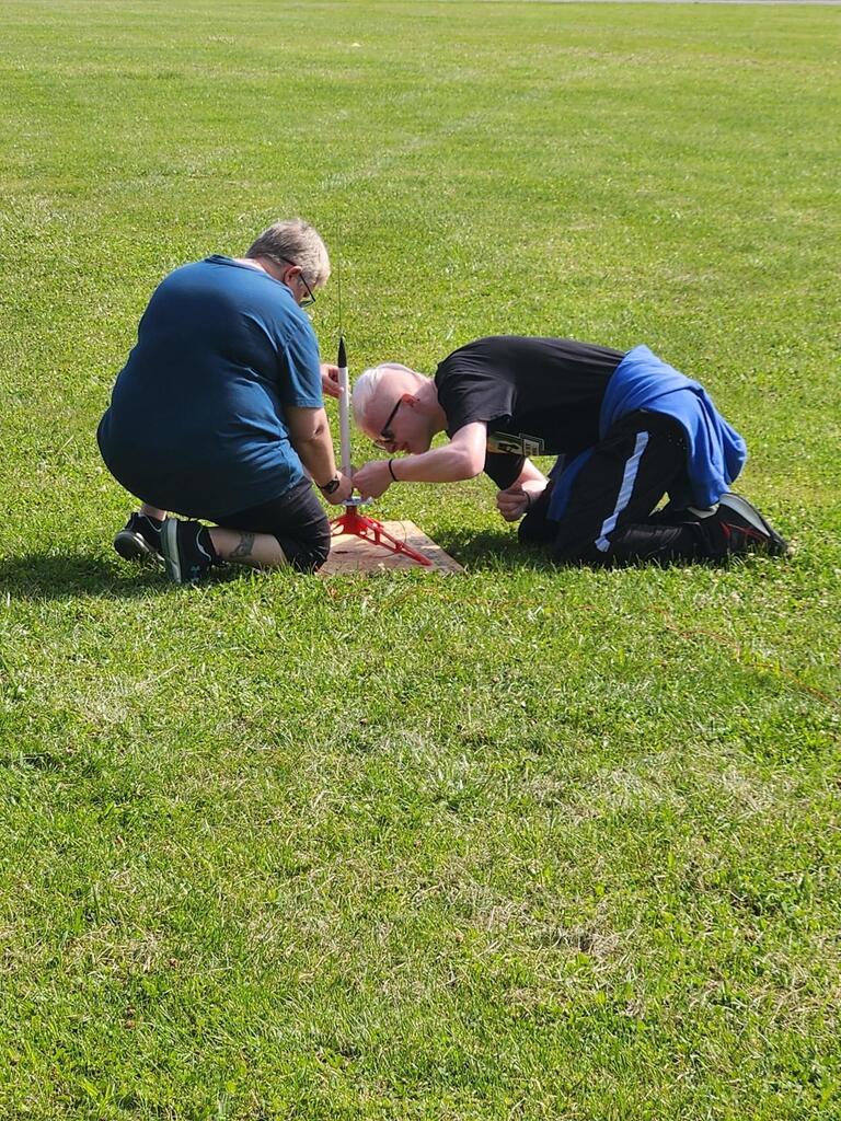 Coach Biddle kneels down beside Eli, a rocketry team member as they assemble his rocket onto the launch pad.