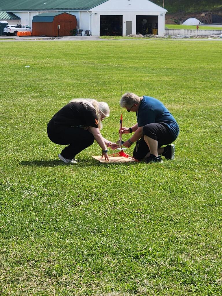 Coach Biddle and Audrey kneel down as they assemble her rocket to the launch pad.