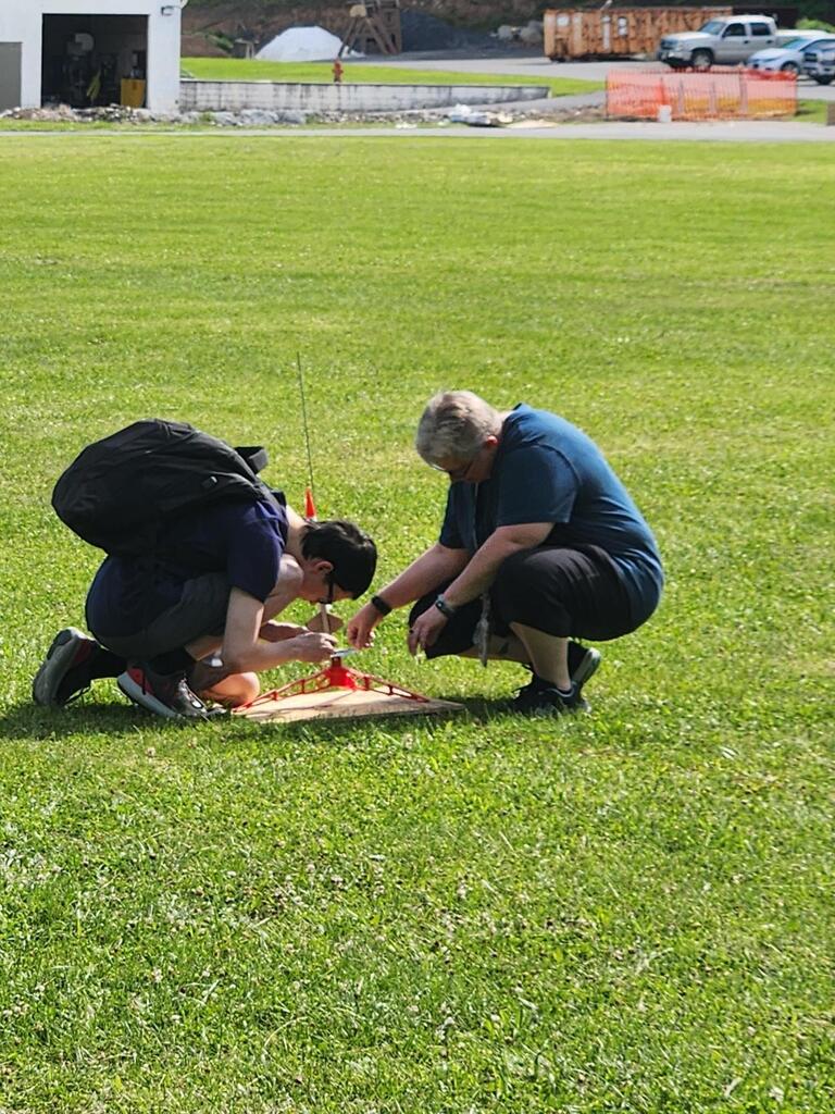 Coach Biddle kneels down with Jason as they assemble his rocket to the launch pad.