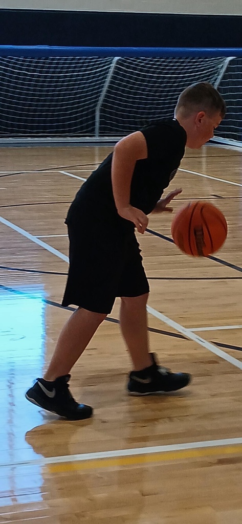 A male camp participant dribbles an orange basketball down the gymnasium court.