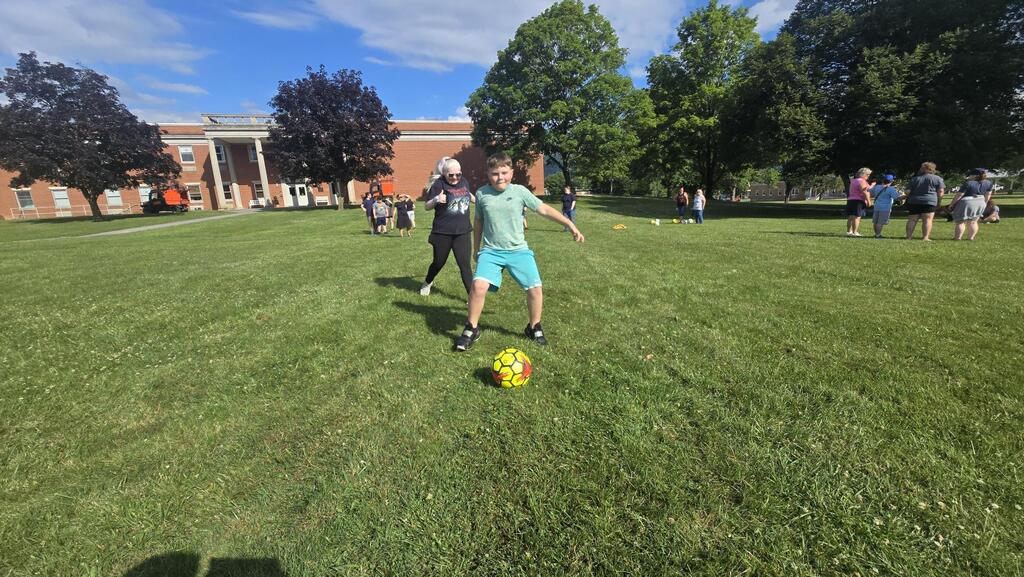 A male camp participant dribbles a neon yellow soccer ball down a field.
