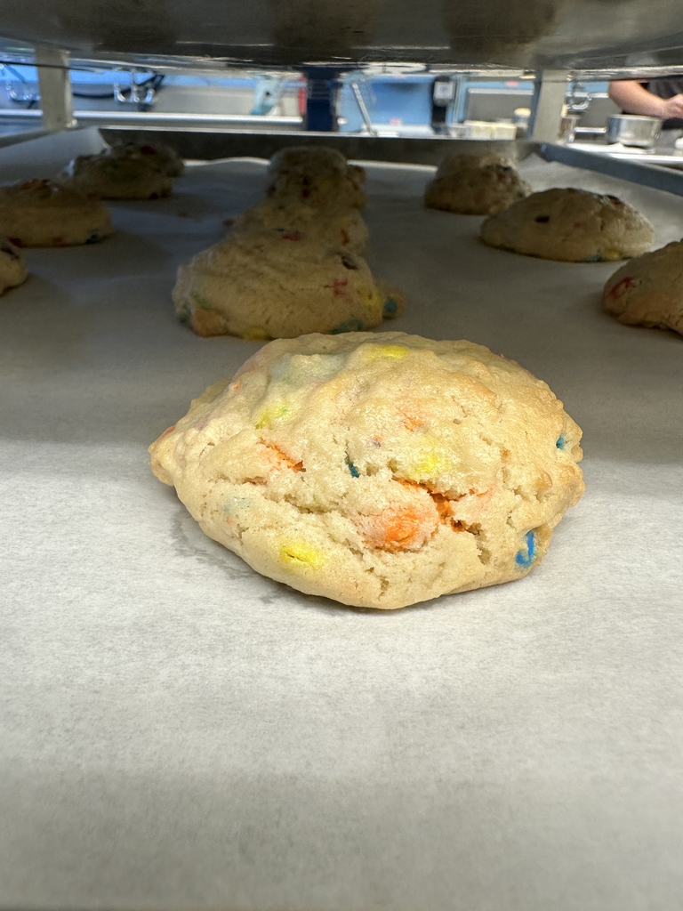 Up-close of M&M cookies on a baking sheet. The cookies have hints of orange, yellow, and blue from the M&M's.
