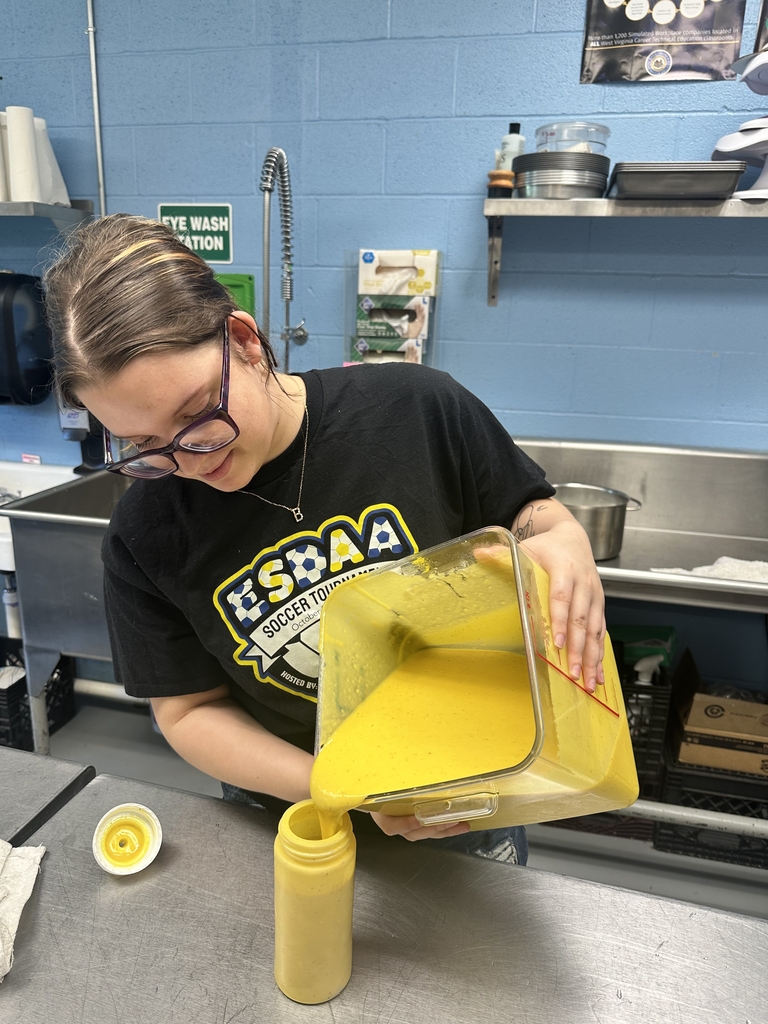 Bindi, a female cafe employee looks down as she carefully pours honey mustard from a large plastic container into a sauce bottle.
