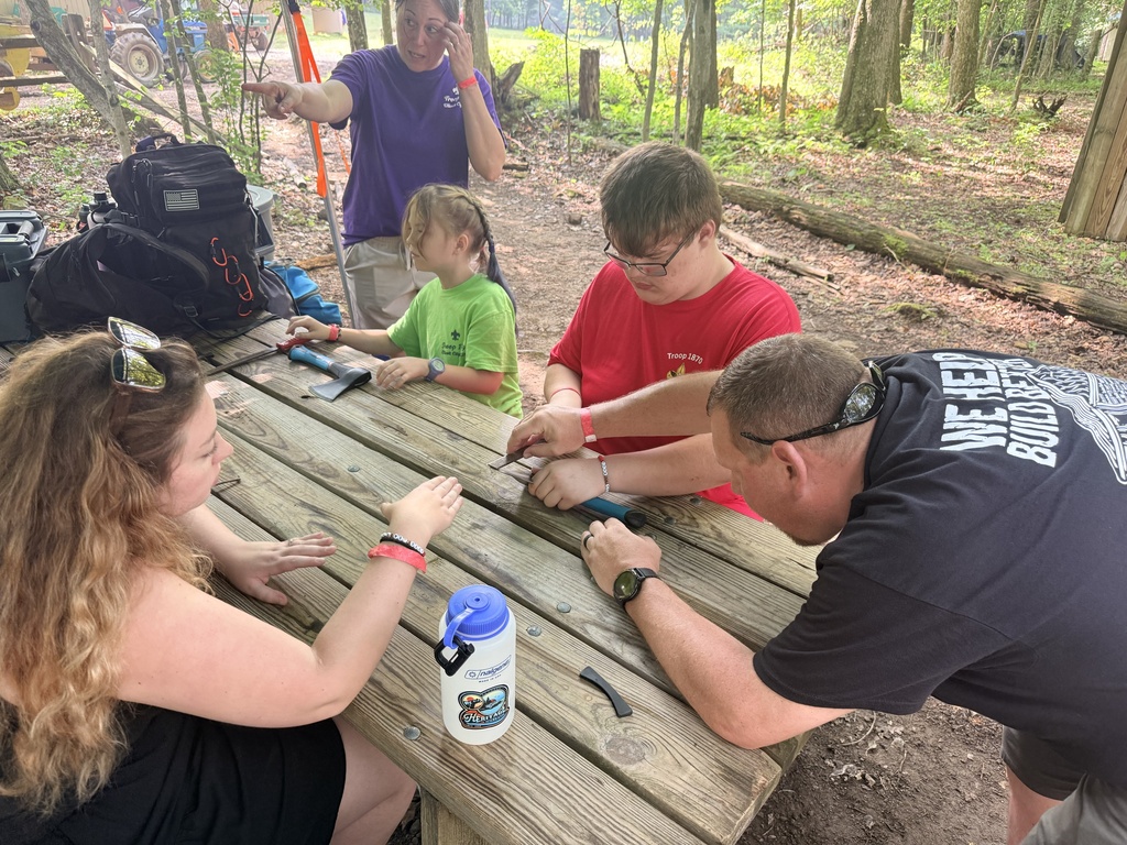 Scout members are seated at a wooden picnic table as they work on a project together.