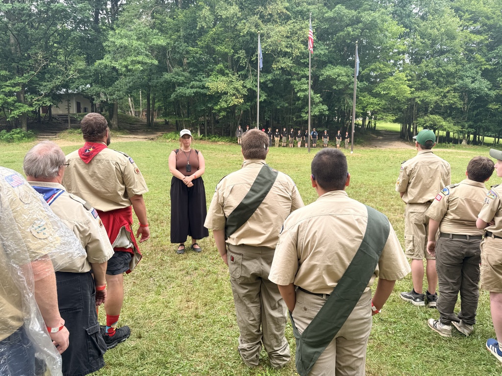 Rows of Boy Scouts dressed in tan-colored Scouting uniforms face towards their Scout leader.