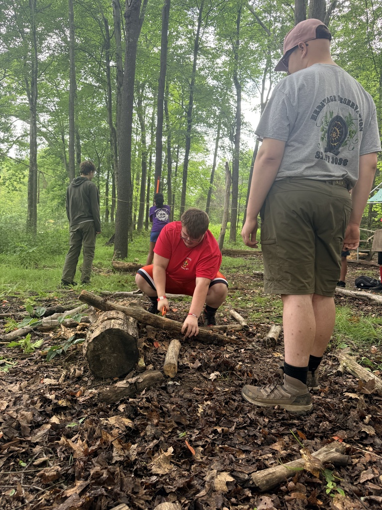 Carson bends down as he saws a piece of wood using a hand saw.