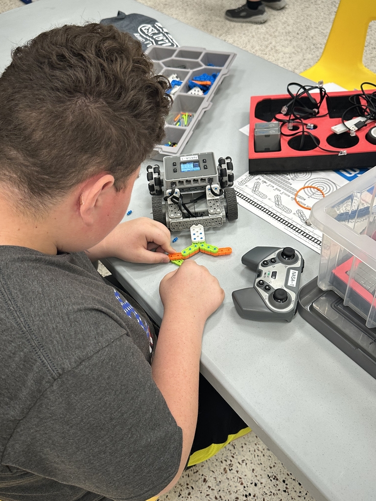 A male camp participant is seated at a table while he builds a VEX robot.