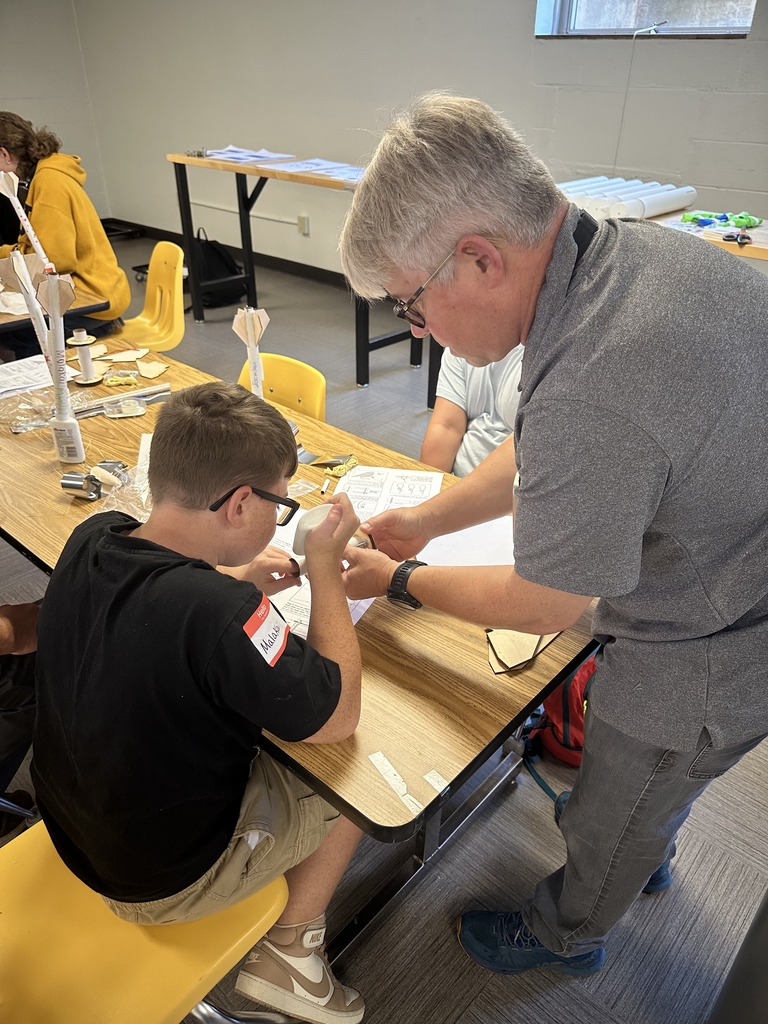 Dr. Ensign assists a male camper with putting glue onto a circular, wooden vessel.
