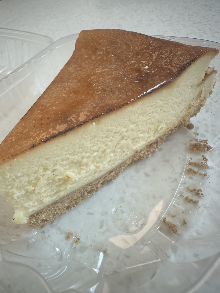 A slice of Crème Brûlée Cheesecake in a clear, plastic container.