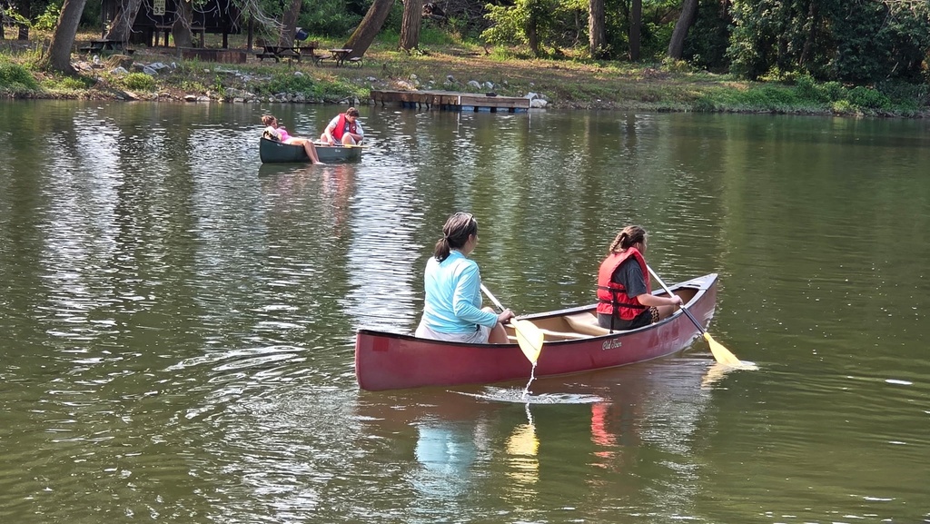 Camp participants in kayaks and canoes are floating and paddling through the river water.