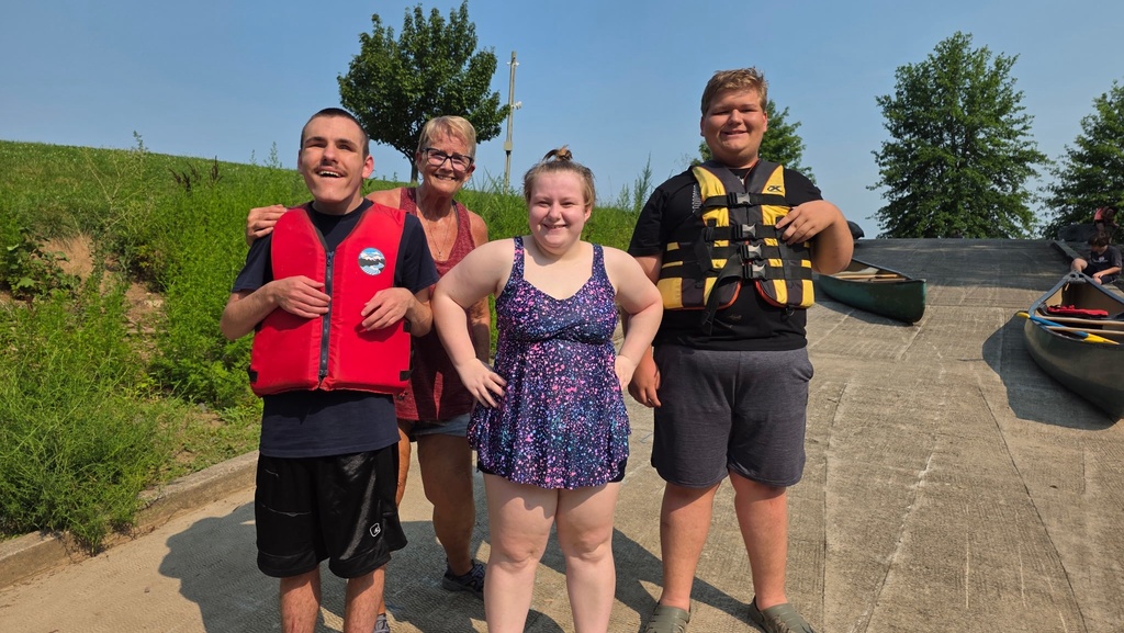 Three summer camp participants stand in a group, wearing life jackets, along with a female residential staff member.