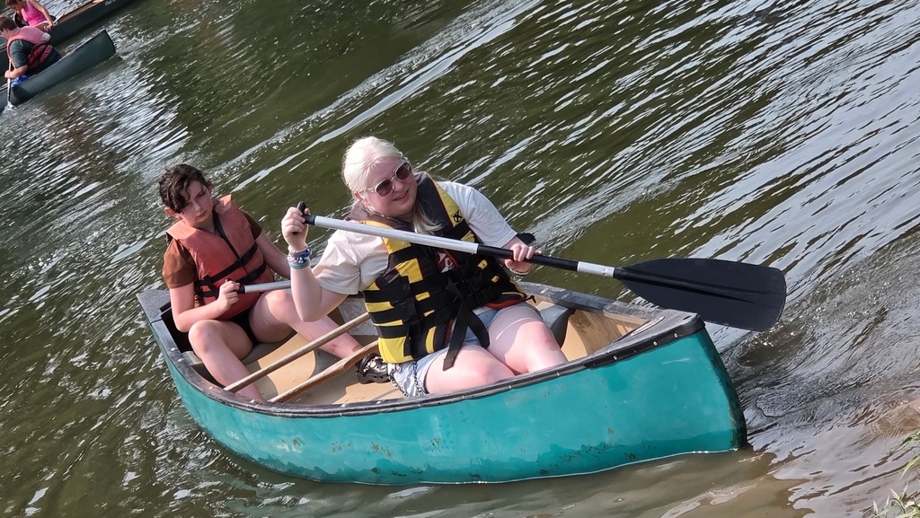 Two female camp participants are seated in a canoe as they paddle through the water.