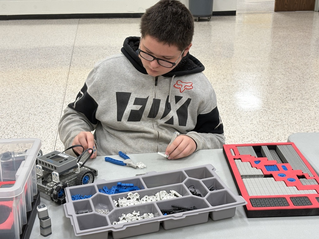 A male camp participant wearing a gray sweatshirt looks down as he builds a VEX robot.