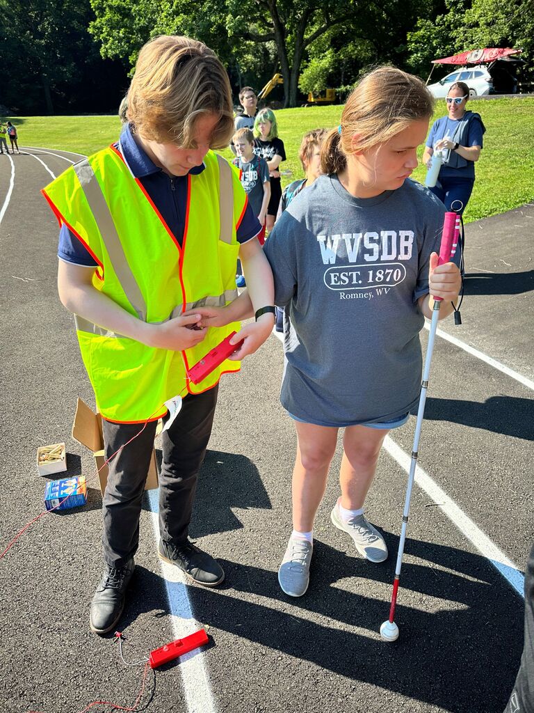 A male camp volunteer guides a female camp participants hand to assist her with pressing the launch button to launch her rocket.
