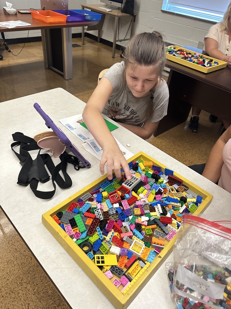 A female camp participant goes to grab a Lego that are scattered inside of a yellow box.