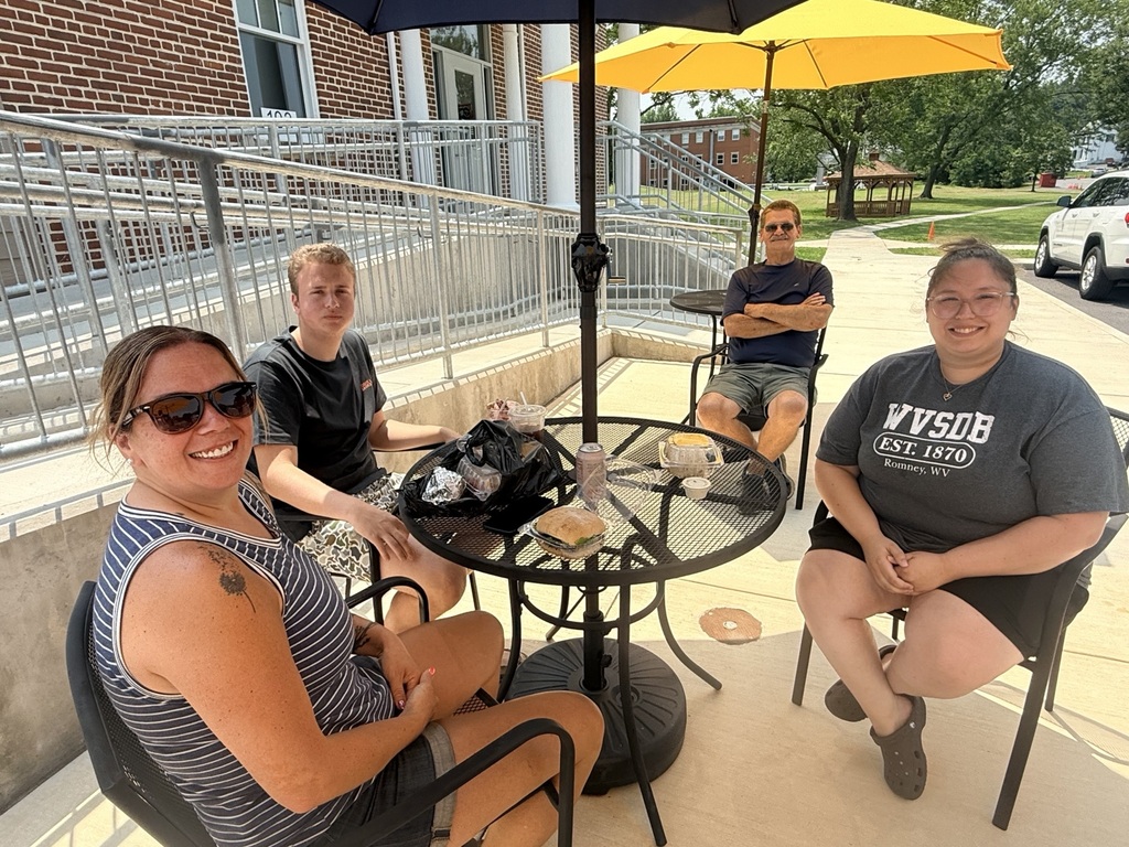 Four attendees smile for a group selfie while enjoying food, drinks, and conversation on the outdoor patio during a Deaf Chat event at Appalachia Provisions Café.
