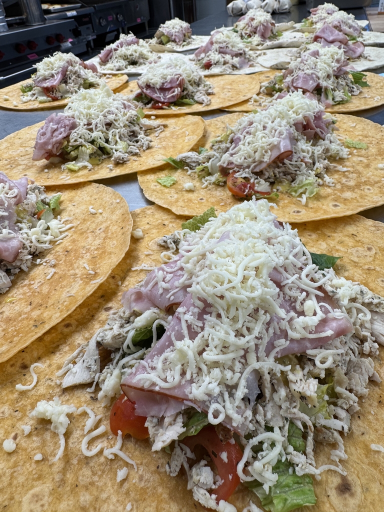 Rows of freshly prepared Chicken Cordon Bleu wraps filled with chicken, ham, lettuce, tomato, cheese, and other fresh ingredients before being folded and served.