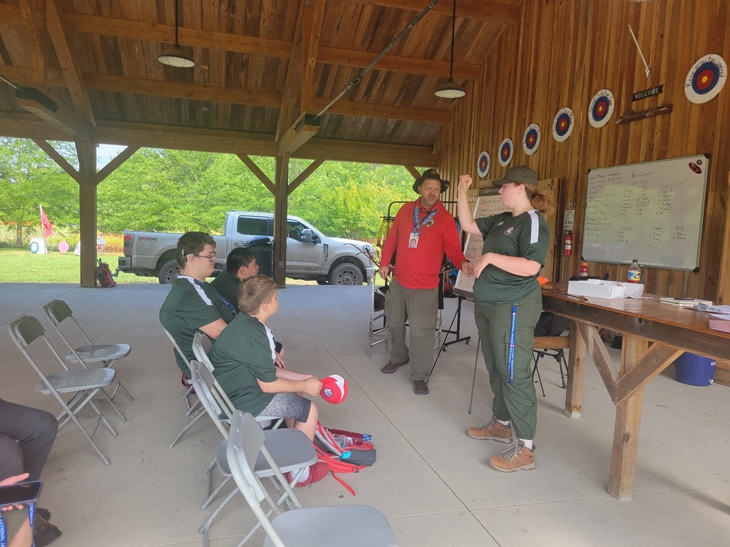 Scouts attend an archery and crossbow safety briefing at the National Jamboree as an instructor demonstrates proper technique inside an open-air pavilion.