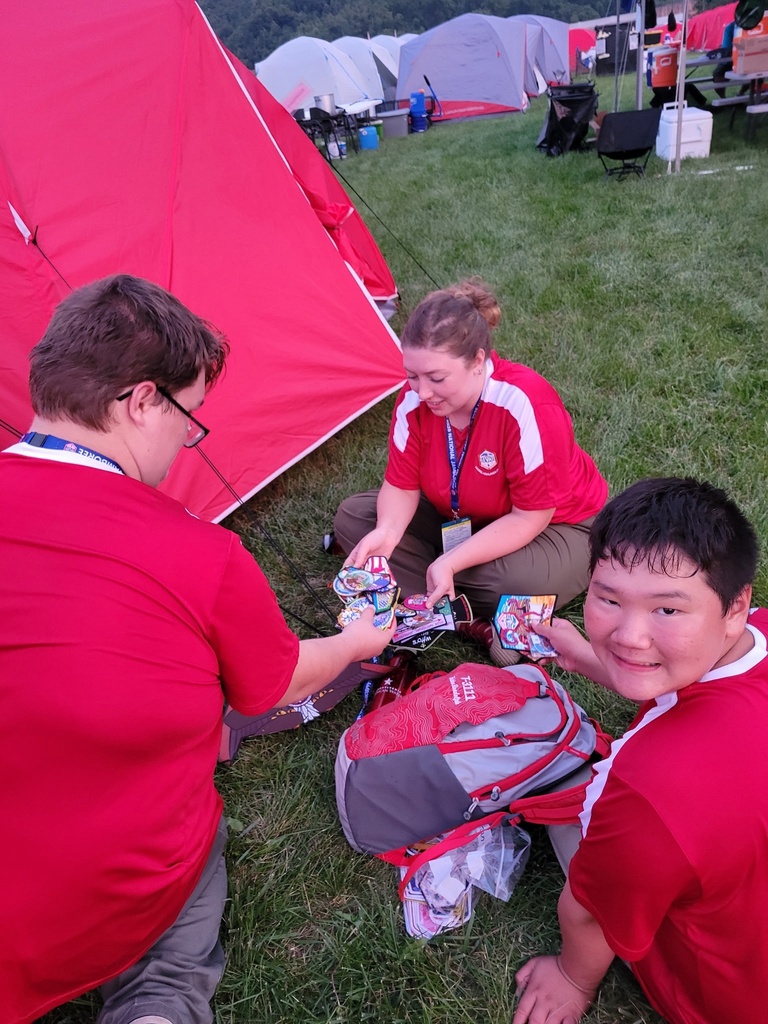 Scouts sit outside their campsite in the evening, smiling as they trade patches and enjoy time together after a full day of activities.