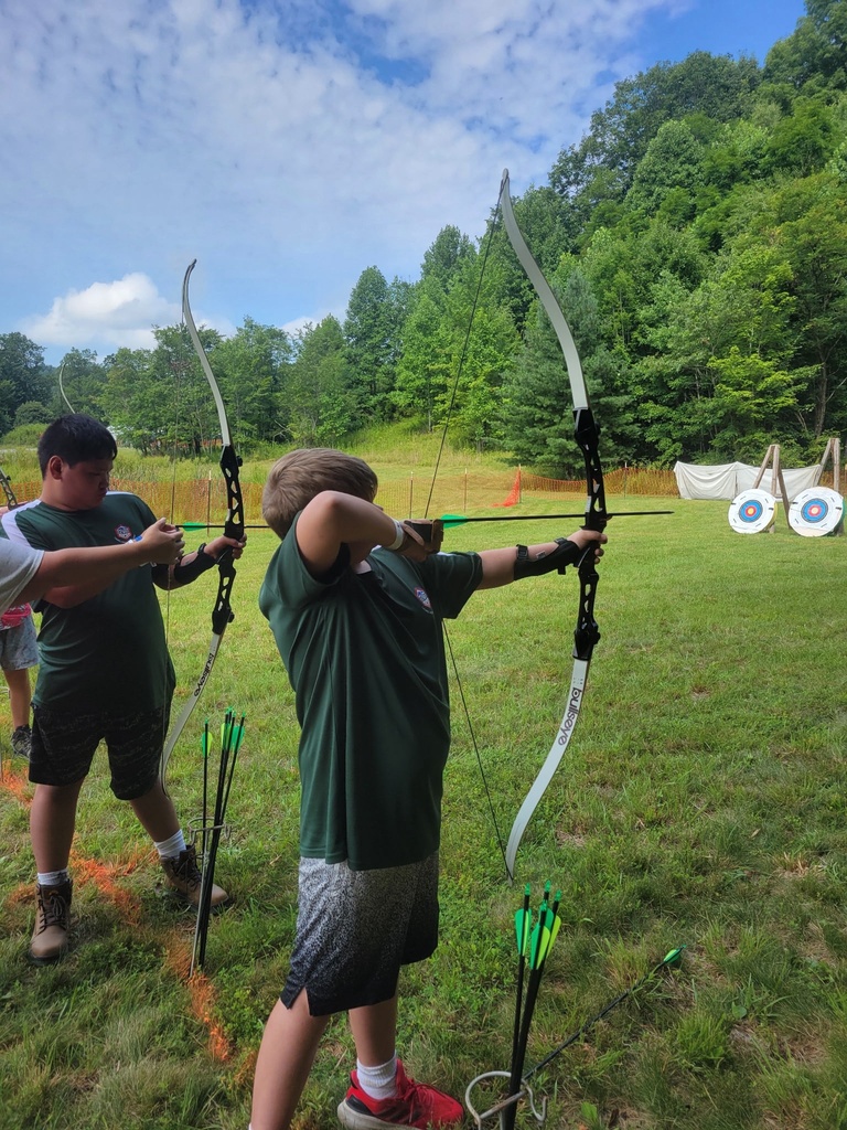 Two Scouts stand side by side on the archery range, drawing recurve bows toward targets during National Jamboree activities.