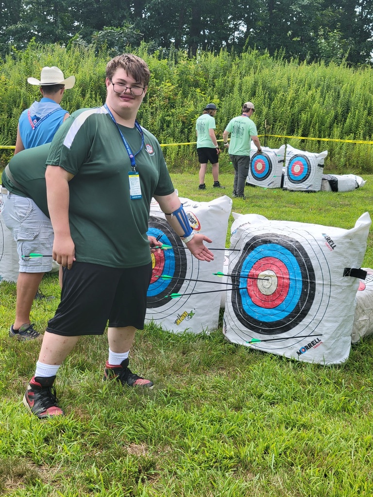 A Scout smiles beside an archery target displaying a tight grouping of arrows after completing a round at the National Jamboree.