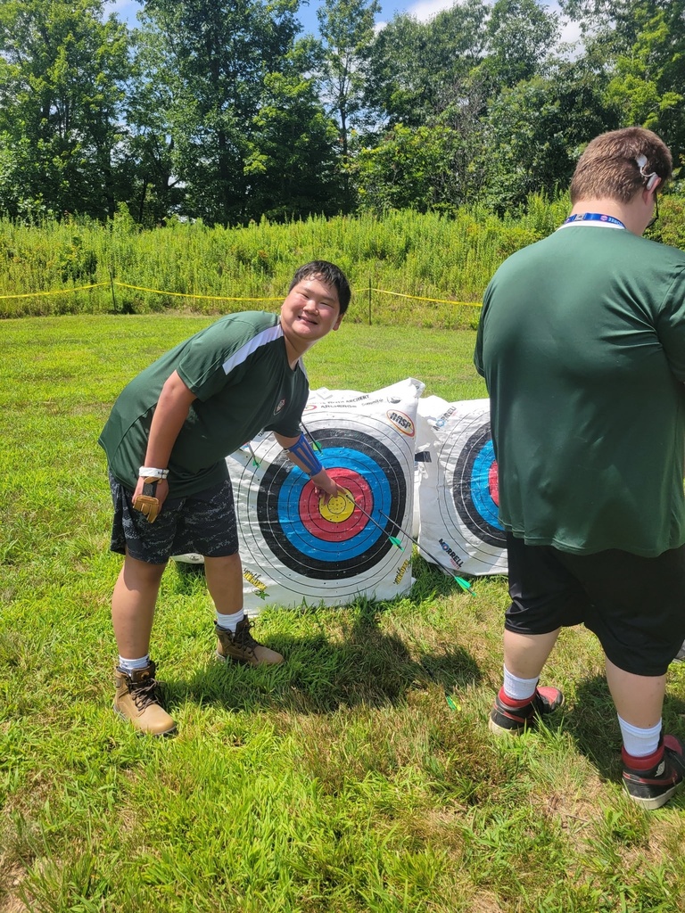 A smiling Scout points to several arrows grouped near the center of an archery target after a successful round at the National Jamboree.
