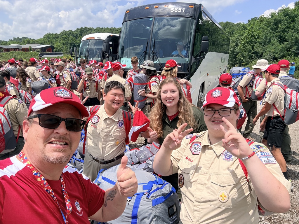 Scouts and leaders gather with backpacks beside buses after arriving at the National Jamboree, excited to begin the week's adventures.