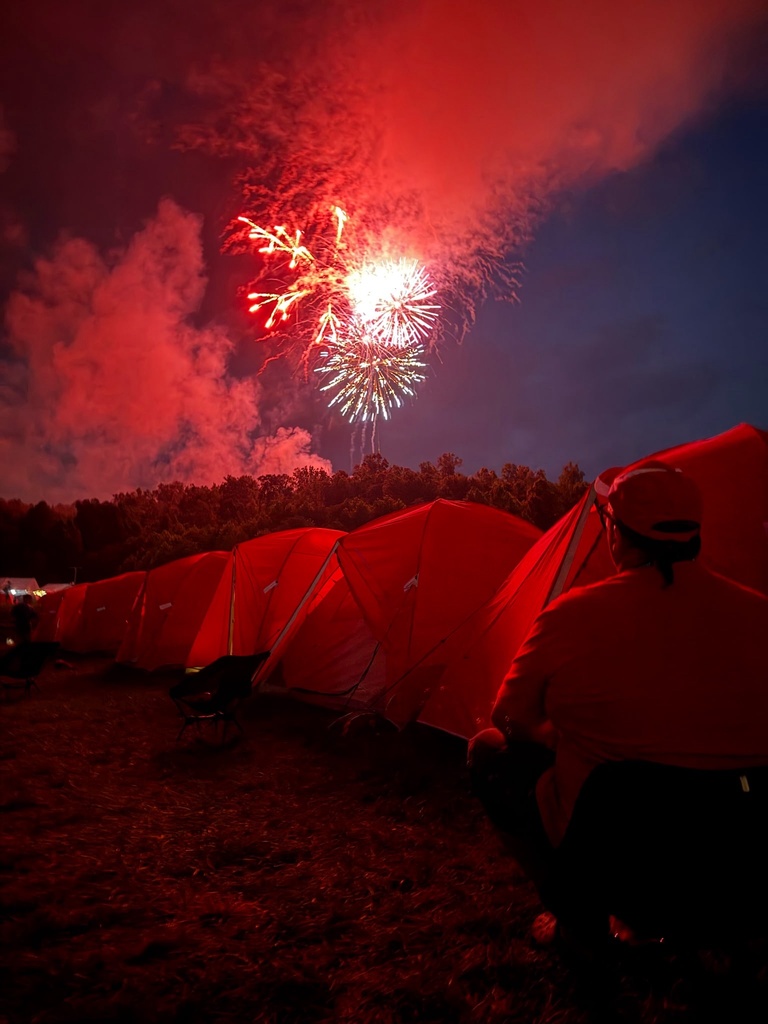 Bright fireworks light up the night sky above rows of camping tents at the National Scout Jamboree.