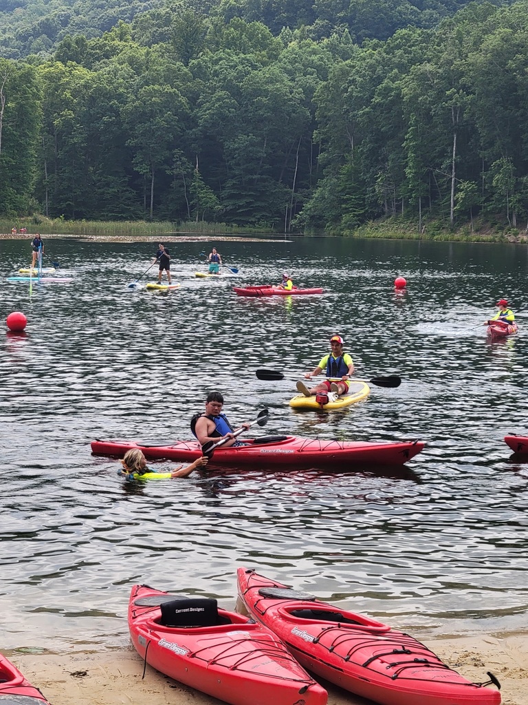 WVSDB Boy Scouts kayak and paddle board on a scenic lake as instructors and other Scouts participate in water activities.