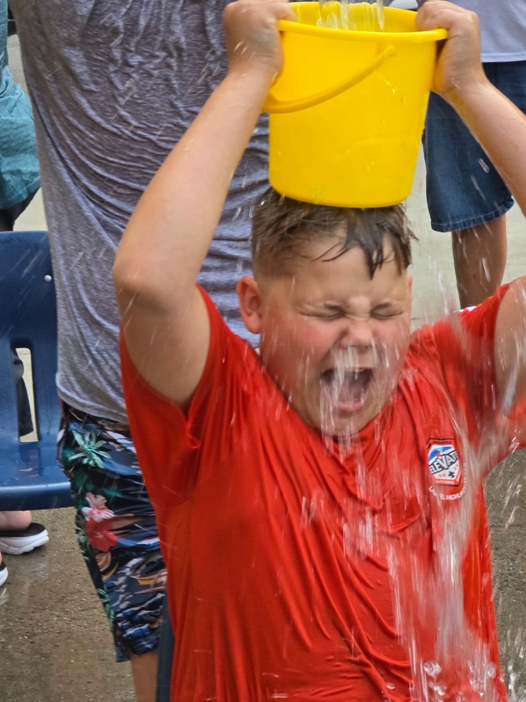 Student laughs as water is poured over their head from a bright yellow bucket during an outdoor Residential Life activity.