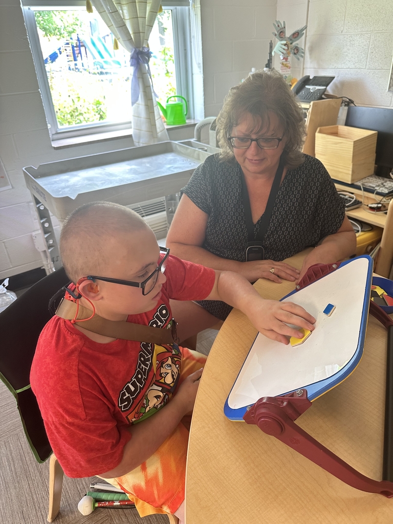 Student uses a slant board and large tactile learning materials while an intervenor observes and provides individualized instruction in a classroom.