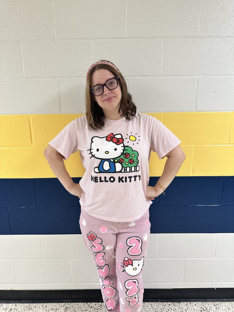 Student smiles while posing in a pink Hello Kitty outfit against a blue, gold, and white hallway wall on campus.
