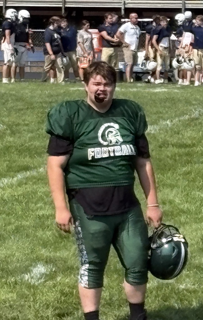 WVSDB student #76 stands on the football field wearing his green Hampshire High School football uniform and holding his helmet after coming off the field.