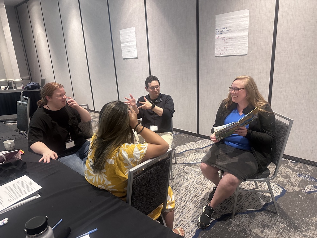 Interpreter Summit participants smile, converse, and participate in a small-group learning activity around a table.