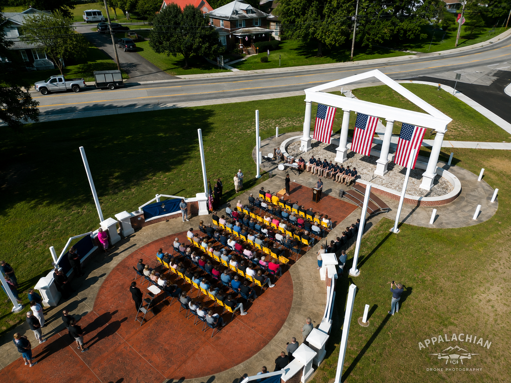 Aerial view of the Administration Building Memorial dedication, showing guests seated in front of the memorial beneath three large American flags.