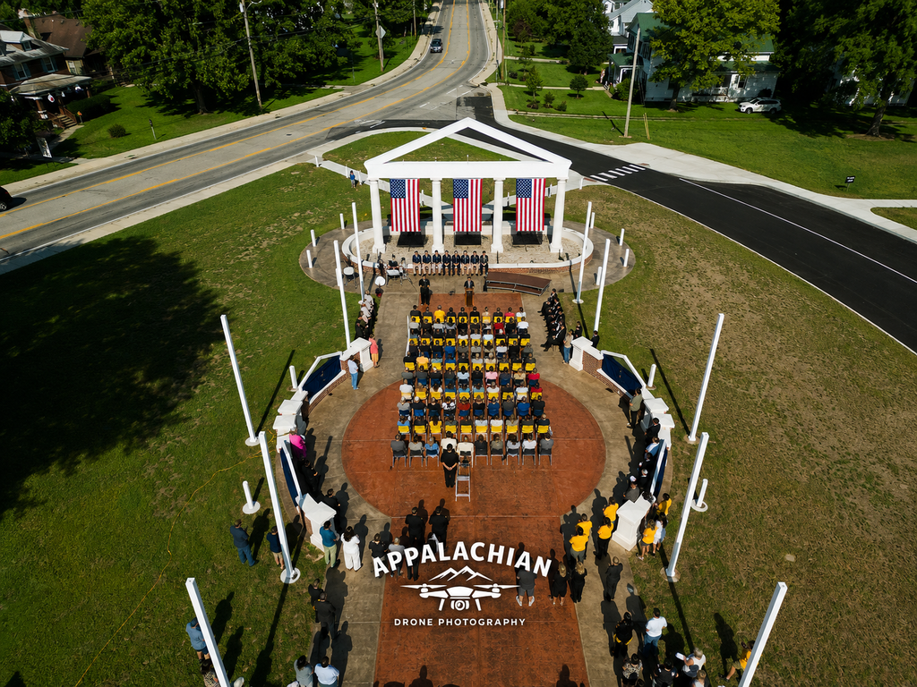 Aerial view looking toward the crowd from behind the Administration Building Memorial, with three American flags hanging between its columns.