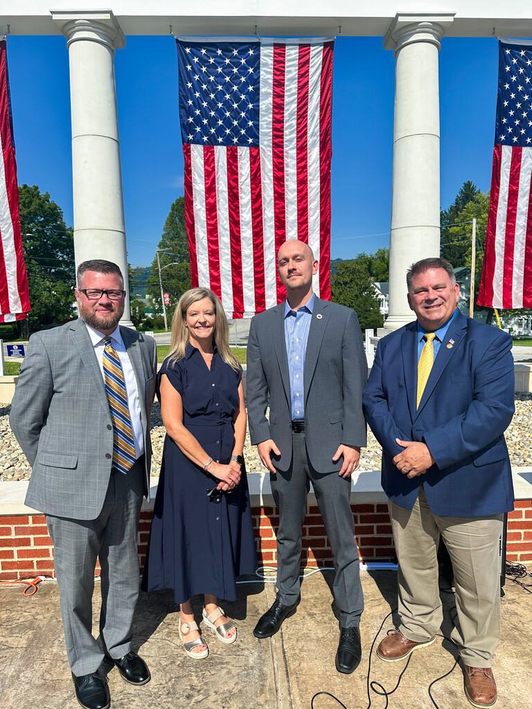 Four special guests stand together for a photo in front of the Administration Building Memorial and American flags.