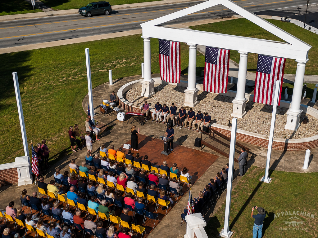 Aerial view from behind the Administration Building Memorial showing the ceremony, surrounding campus grounds, and parking area.
