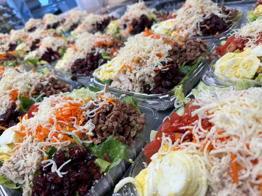 Close-up of freshly prepared cranberry pecan grilled chicken salads with lettuce, chicken, dried cranberries, pecans, shredded cheese, carrots, tomatoes, cucumbers, and hard-boiled eggs.