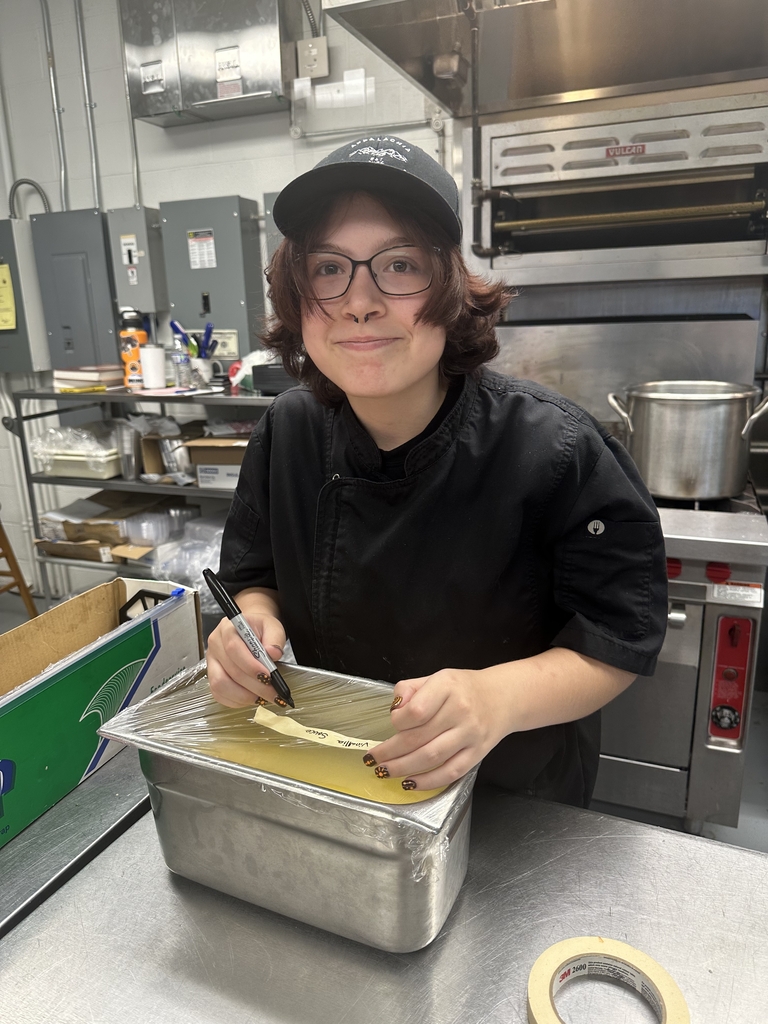 Student in an Appalachia Provisions uniform labels a covered food container in the café kitchen.