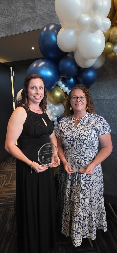 Ms. Heather Hartman and Mrs. Joanna Gilbert smile while holding their finalist awards at the West Virginia Teacher and Service Personnel of the Year celebration. Blue, white, and gold balloons are displayed behind them.