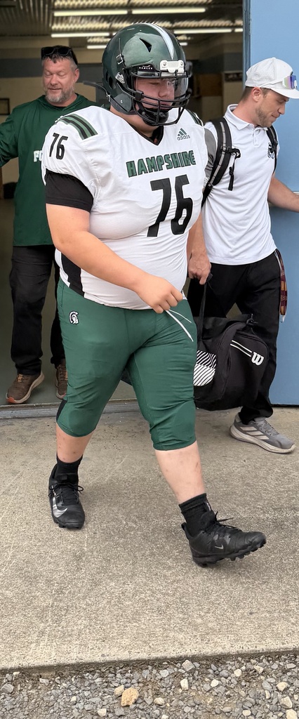 WVSDB student Carson, wearing number 76, walks outside in his green and white Hampshire High School football uniform and helmet before a game.