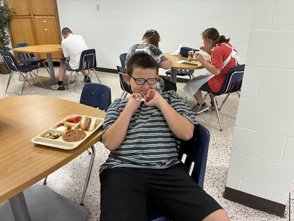 A WVSDB student smiles while seated at a cafeteria table with a picnic meal in front of him.