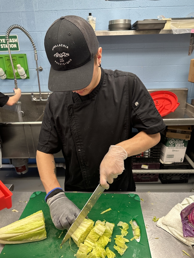 Appalachia Provisions culinary student in a black chef uniform chops romaine lettuce on a green cutting board while preparing food in the café kitchen.