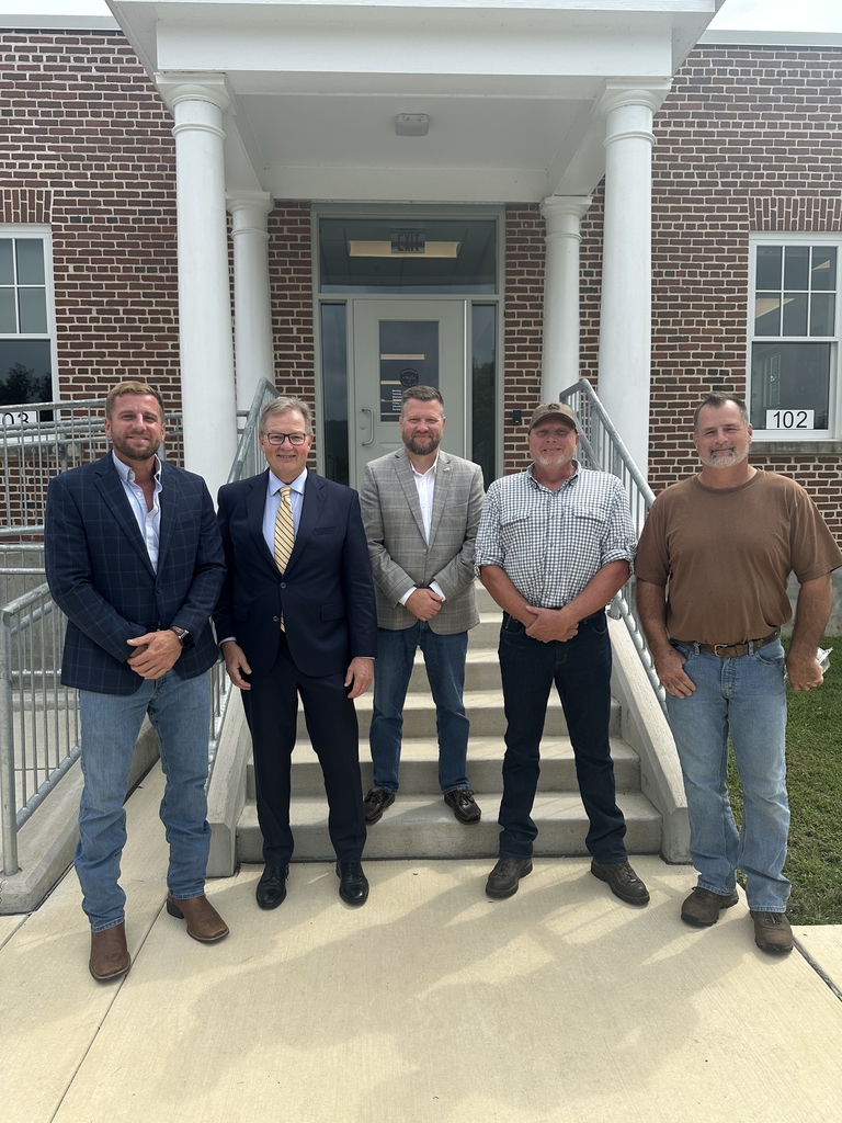 Five men stand together outside a brick campus building with white columns following a visit to WVSDB.
